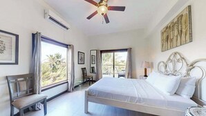 A bedroom with a bed, a ceiling fan, a window, and a chair. - Serene oceanfront condo with shared pool, ocean view, WiFi, & partial AC (San Pedro)