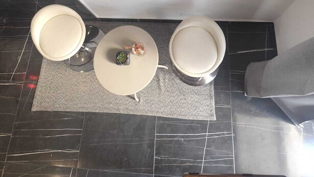 A room with a black and white photograph on the wall, two white stools, a small table with a decorative item, and a patterned rug. - CasaRì Vacation Rental – Apartment in the Heart of Bari (Bari)