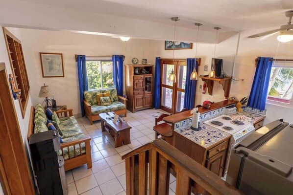 Una sala de estar con sofá, mesa de centro, televisor y una zona de cocina con estufa y refrigerador.