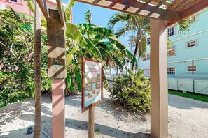A covered outdoor area with a signboard, palm trees, and a building in the background. - Ocean-view condo with pool, immediate beach access & partial AC (San Pedro)