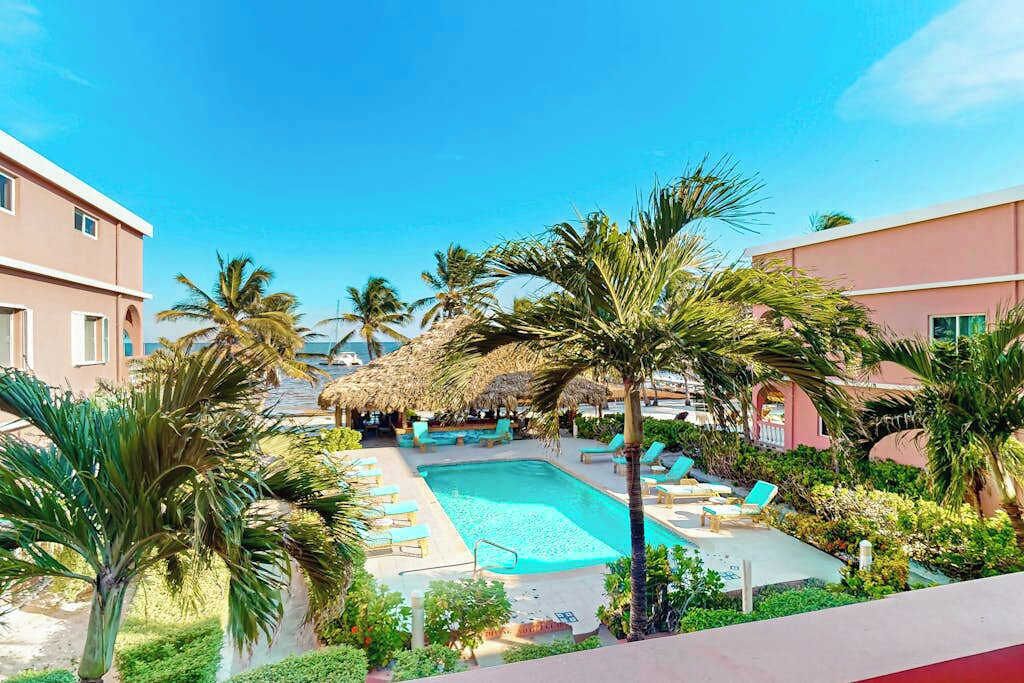 Ein Swimmingpool, umgeben von Palmen und Liegestühlen, mit Gebäuden im Hintergrund.