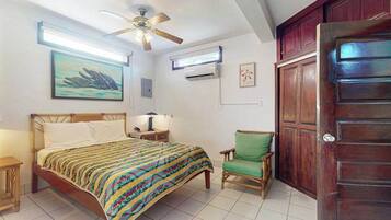 Een slaapkamer met een bed, een plafondventilator, een airconditioningapparaat, een stoel en een houten deur.