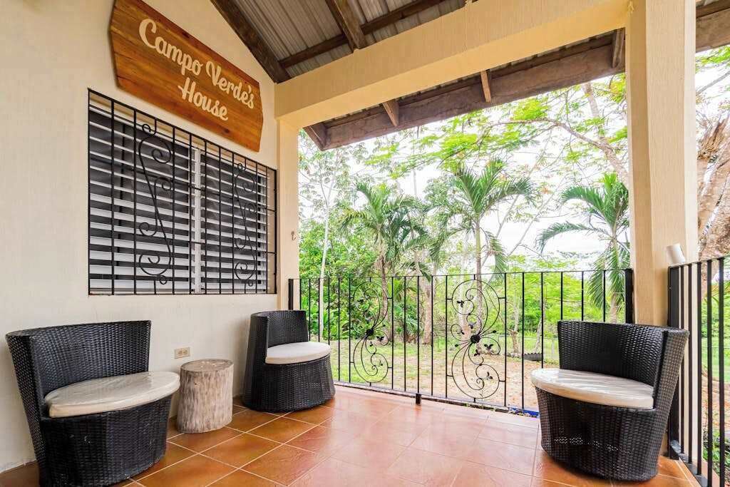 A covered patio area with wicker furniture, a metal gate, and a sign reading 'Campo Verde's House.'