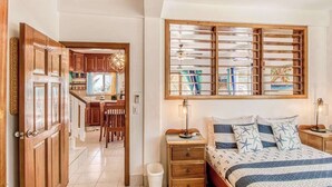 A bedroom with a bed, bedside tables, a window with blinds, and a view of the kitchen. - Beachfront condo with beach access, dock, pool, balcony, & ocean views (San Pedro)