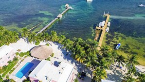 An aerial view of a resort with a swimming pool, palm trees, a pier, and boats. - Beachfront condo with beach access, dock, pool, balcony, & ocean views (San Pedro)