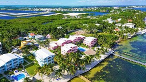 An aerial view of a coastal resort with multiple buildings, a swimming pool, and a clear view of the ocean. - Beachfront condo with beach access, dock, pool, balcony, & ocean views (San Pedro)