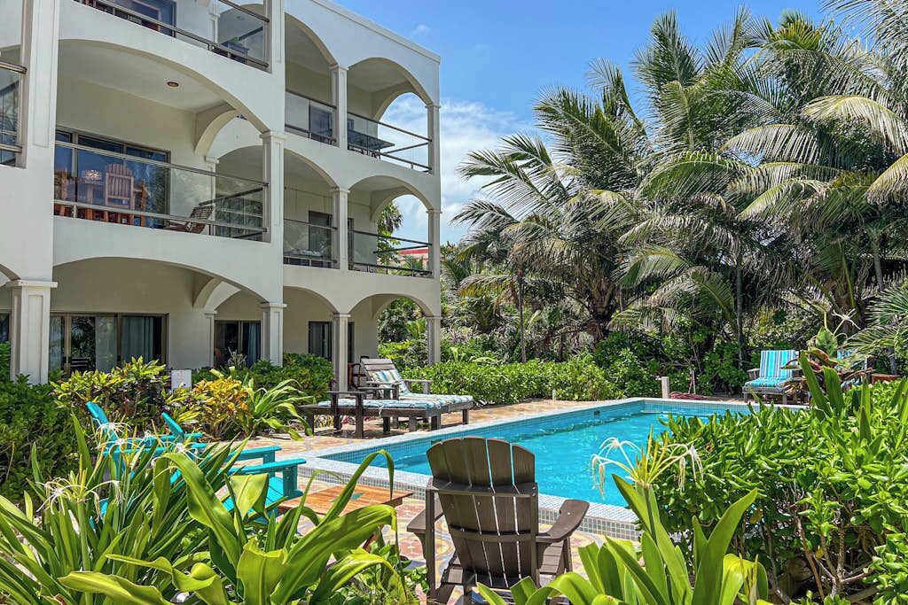 Un hotel de varios pisos con piscina rodeada de exuberante follaje y palmeras.
