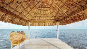 Une terrasse en bois, surmontée d’un toit de chaume, et un banc en bois d’où l’on peut admirer la mer.