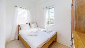 Een slaapkamer met een houten bed, wit beddengoed, een raam met zonwering, en een houten garderobe.
