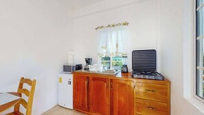 Een kleine keuken met een magnetron, een gasfornuis, houten kastjes en een raam met gordijnen.