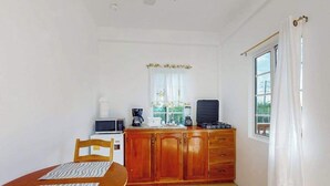 Een kleine keuken met een houten tafel, een magnetron, een koffiezetapparaat en een raam met gordijnen.