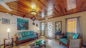 Uma sala de estar com teto de madeira, um sofá, uma poltrona, uma mesa de centro e obras de arte nas paredes.