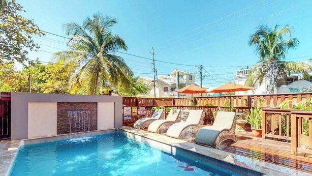 Uma piscina com espreguiçadeiras e guarda-sóis, cercada por um deck de madeira e palmeiras.