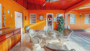 Um espaço interno com ventilador de teto, mesa redonda de vidro cercada por cadeiras de vime, um armário de madeira e uma árvore de Natal.