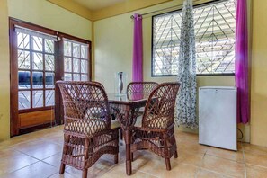 A dining area with wicker chairs, a glass table, a refrigerator, and a window with curtains. - A new home in a great neighborhood w WiFi, AC - near Maya ruins (San Ignacio)