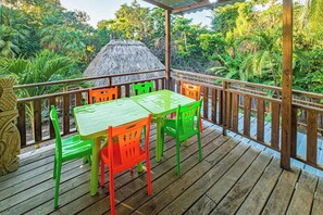 A wooden deck with a table and chairs, surrounded by lush greenery. - Spacious coastal house with outdoor pool, deck & near beach (Placencia)
