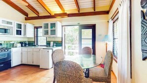 A kitchen with white cabinets, a stove, and a dining area with wicker chairs. - Oceanfront retreat with water view, pool, AC & free WiFi - easy beach access (Placencia)