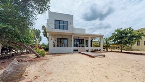 Una casa moderna de dos pisos con un porche cubierto y un patio arenoso.