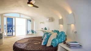 A bedroom with a curved bed, a ceiling fan, a view through a sliding door, and a bedside table with books. - Lagoon-front studio with water access, infinity pool, & AC (Placencia)