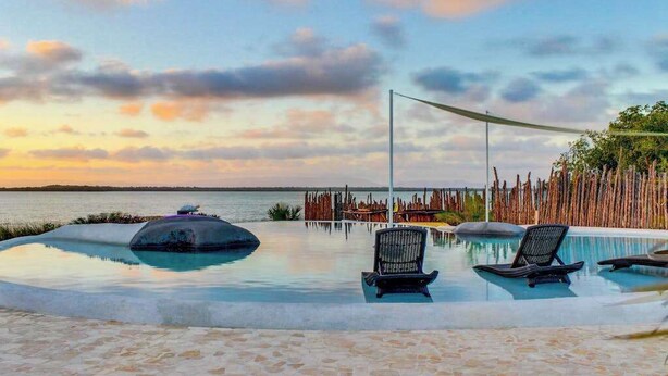 A pool with lounge chairs, a wooden fence, and a view of the sea. - Lagoon-front studio with water access, infinity pool, & AC (Placencia)