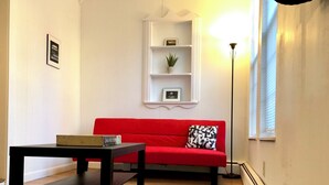 A living room with a red sofa, a black coffee table, a white shelf with a plant, and a floor lamp. - Tiny Home Away From Home - Complete Privacy, Peace (Watertown)