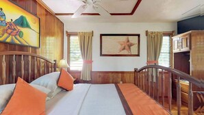 A hotel room with a bed, wooden headboard, a painting, a starfish artwork, and a ceiling fan. - Charming cabana with a porch, hammock, strong WiFi, and a shared pool & grill (Hopkins)