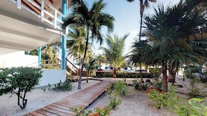 Un resort con terraza de madera, palmeras y un sendero de arena.