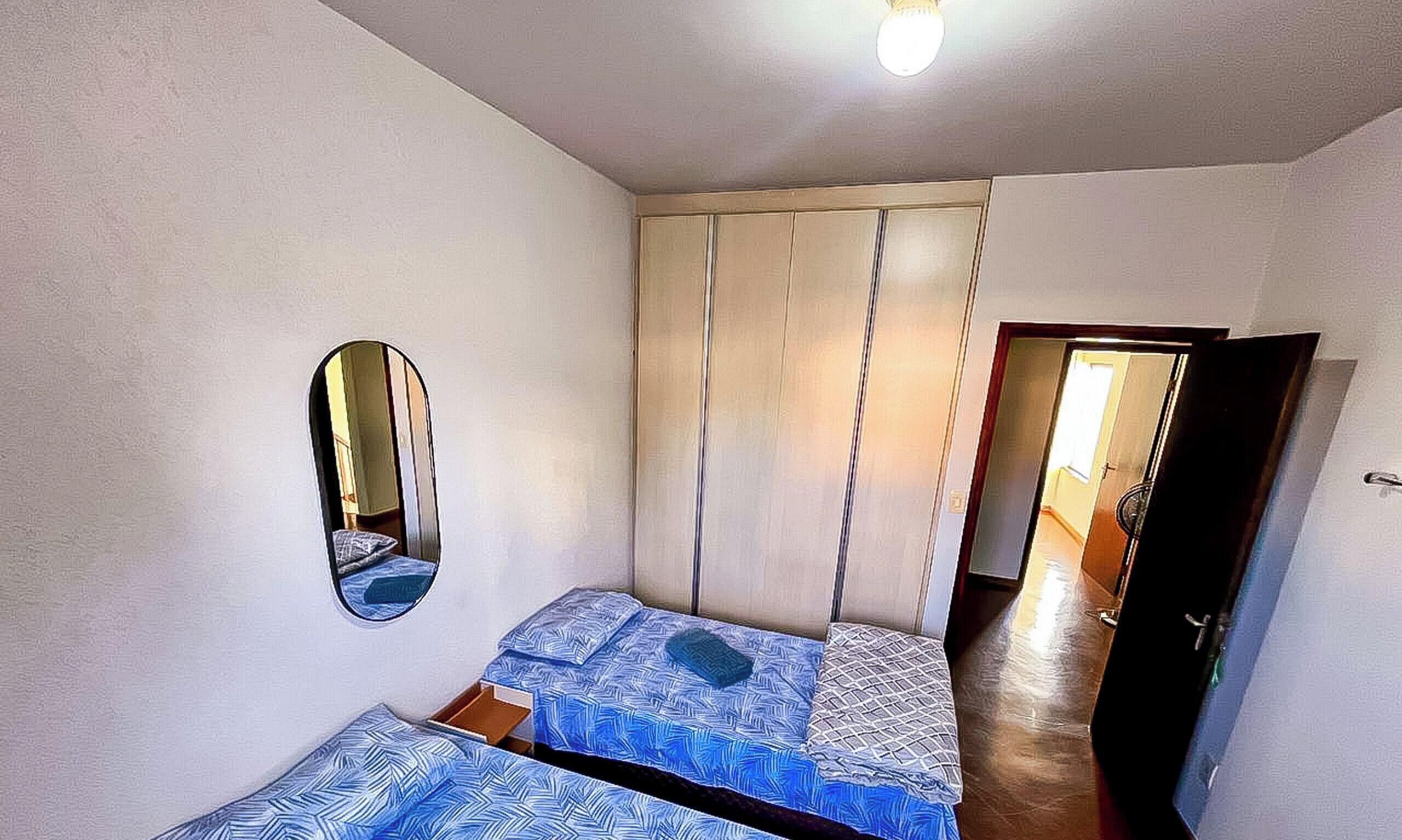 A small room with two beds, a mirror, a wardrobe, and a door leading to another room.