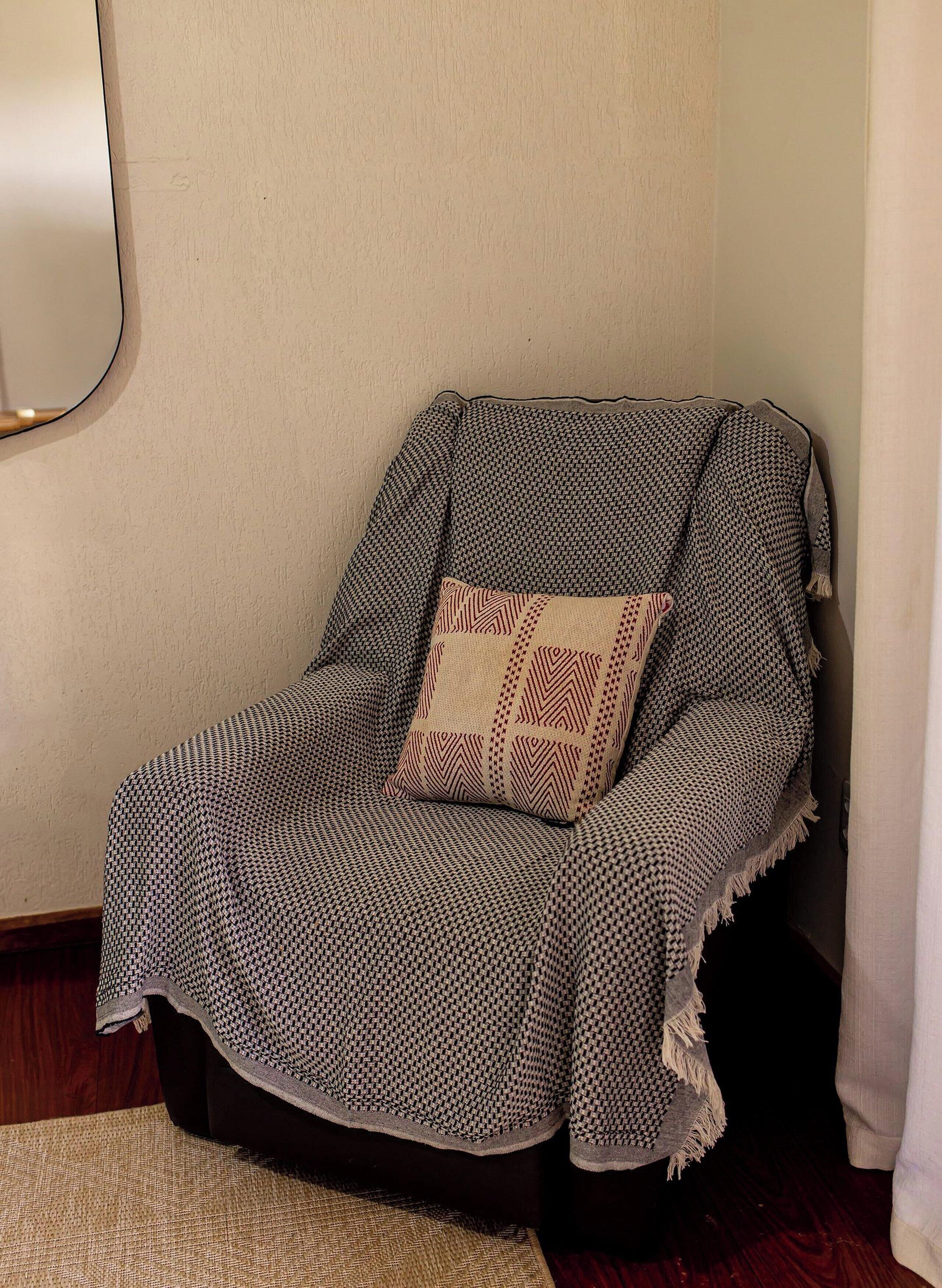 Une pièce d’angle avec un fauteuil recouvert d’une couverture à motifs, un petit tapis et un miroir fixé au mur.