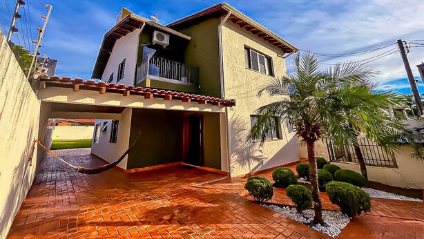 Una casa de dos pisos con balcón, camino de ladrillo y una palmera.