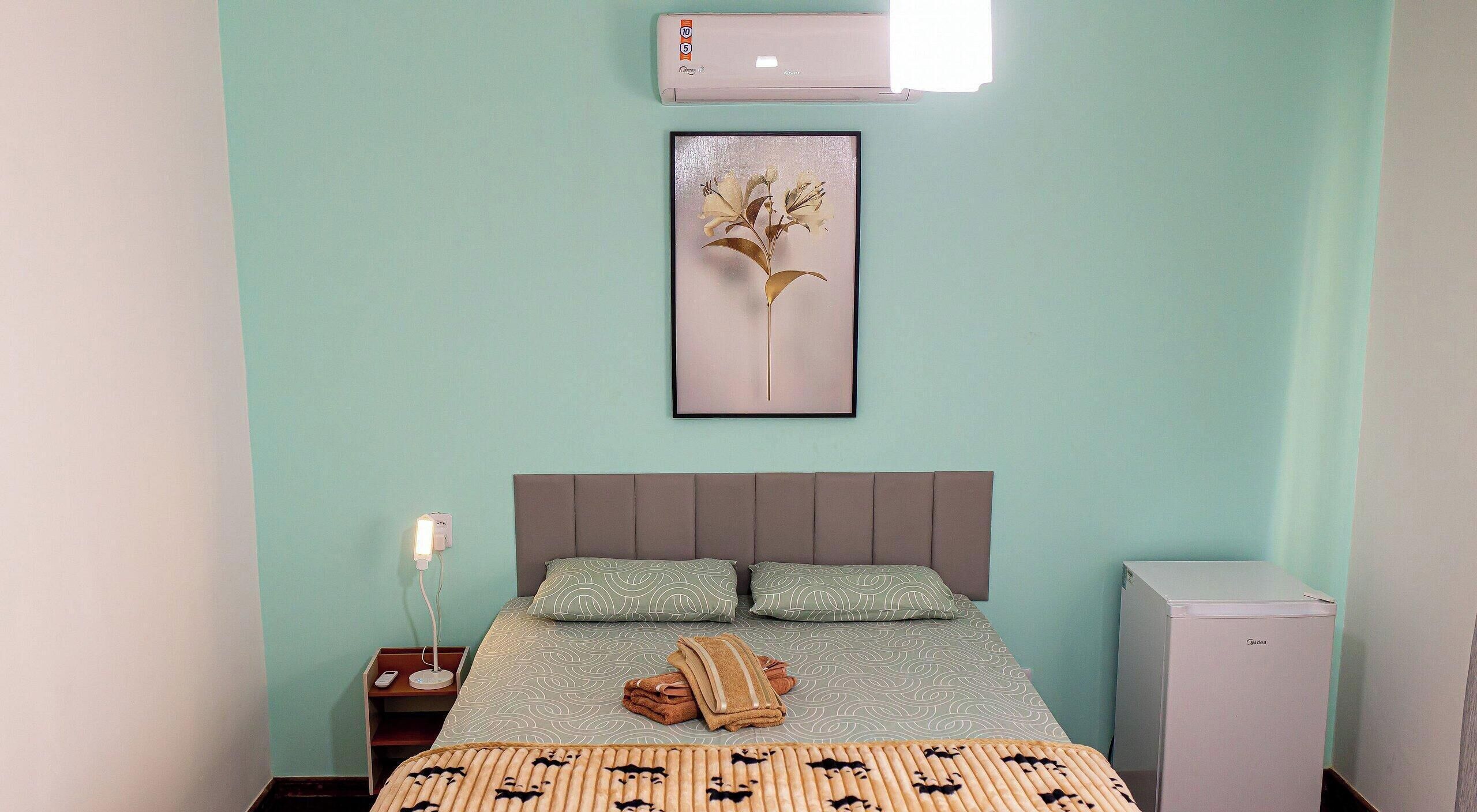 A bedroom with a bed, a nightstand, a wall-mounted air conditioner, and a framed picture.