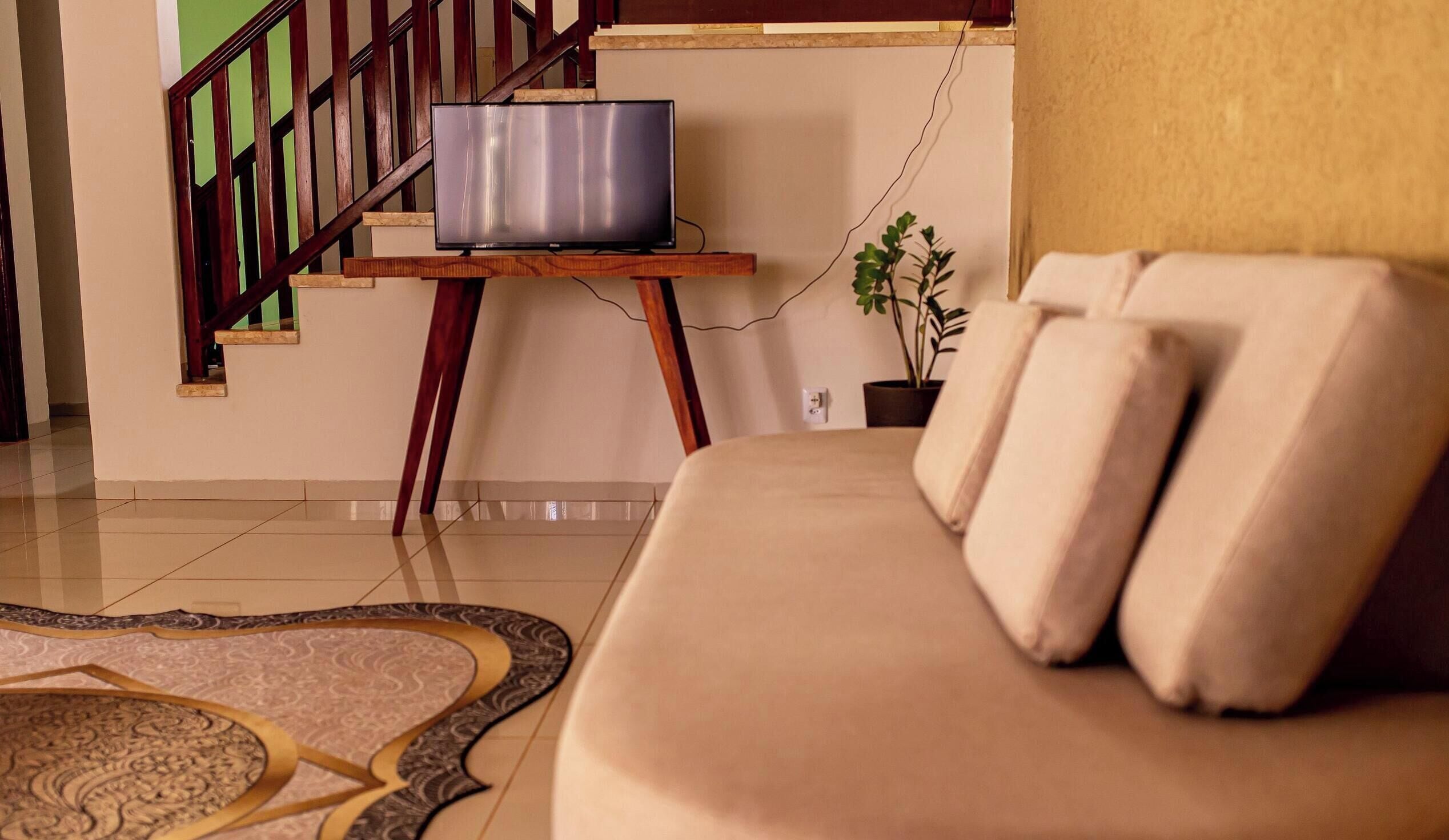 A living room with a sofa, a television on a wooden stand, a staircase, and a potted plant.