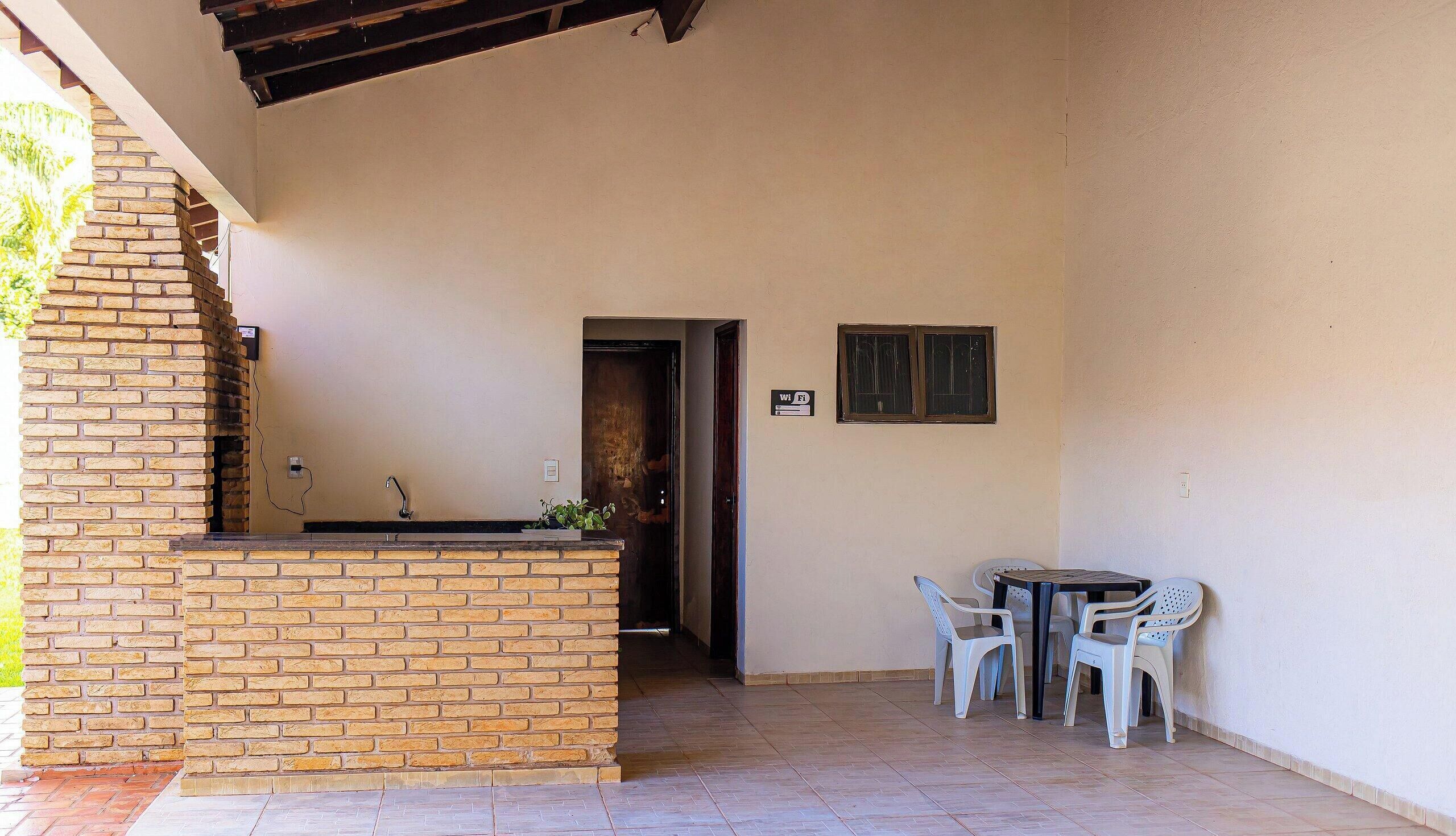 Uma área de pátio com balcão de tijolos, uma mesa com cadeiras e uma porta que dá para o interior.