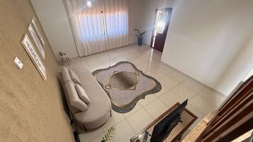 Una sala de estar con un sofá color beige, un tapete estampado, un televisor sobre un mueble bajo y una planta en maceta.