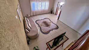 Una sala de estar con sofá, mesa de centro, televisor, alfombra estampada y ventana con cortinas.