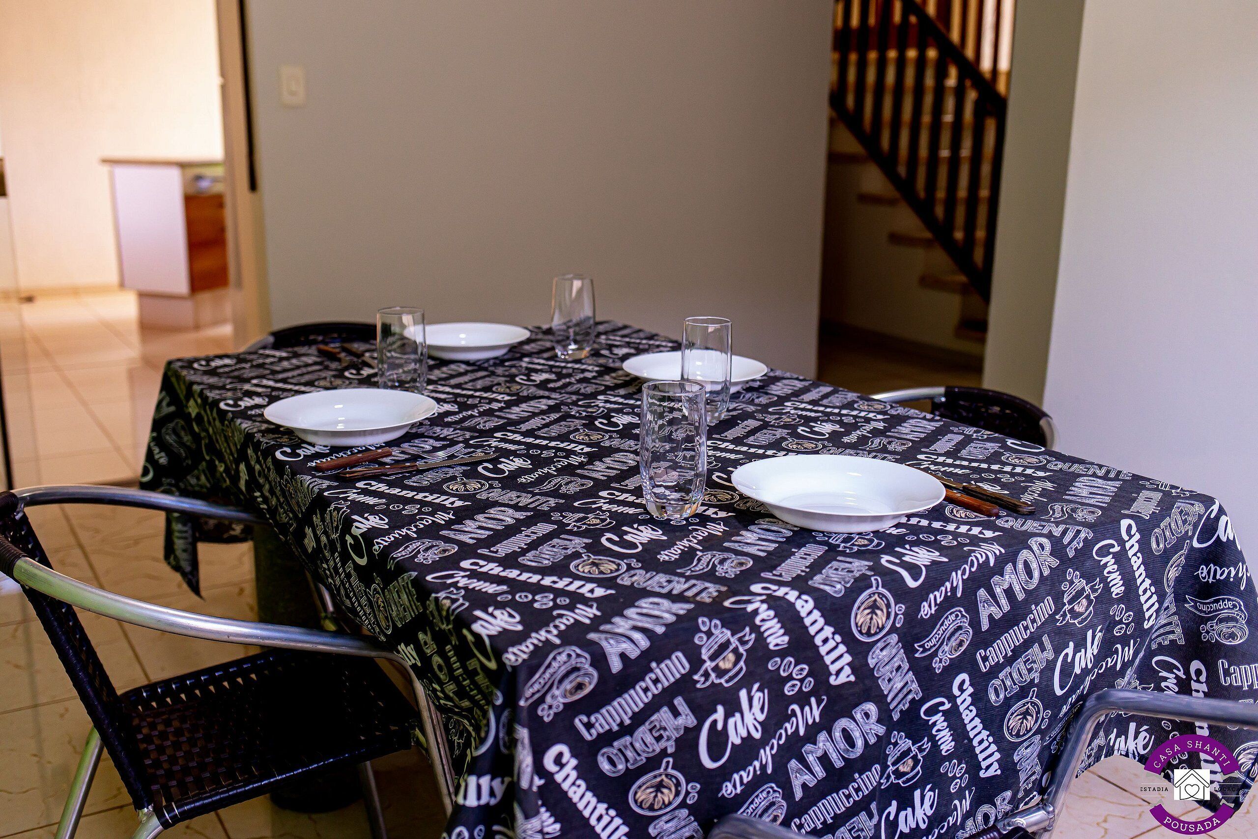 A dining table with a black tablecloth featuring coffee and cake patterns, surrounded by chairs.