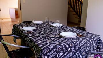 A dining table with a black tablecloth featuring coffee and cake patterns, surrounded by chairs.