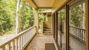 Un balcone coperto con pavimento in pietra, porte in vetro e vista su una zona boschiva.