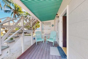 A covered outdoor area with a wooden deck, two chairs, and a staircase leading to a building. - Charming island cabana with central AC, bikes & picnic area near beach (Caye Caulker)
