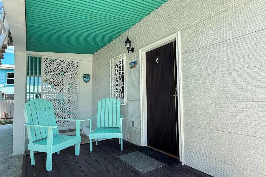 A porch with two turquoise Adirondack chairs, a black door, and a white textured wall.