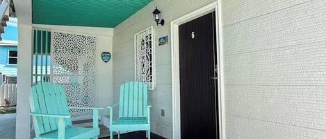 A porch with two turquoise Adirondack chairs, a black door, and a white textured wall.