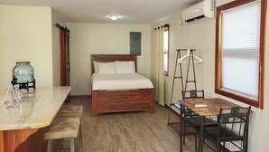 A room with a bed, a desk with a chair, a table with chairs, an air conditioning unit, and a window with blinds. - Beachfront abode with well-equipped kitchen - pool, beach, grill, & canoe access (Caye Caulker)