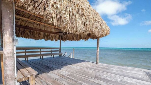 A wooden pier with a thatched roof structure, wooden benches, and a view of the ocean. - Beachfront abode with well-equipped kitchen - pool, beach, grill, & canoe access (Caye Caulker)