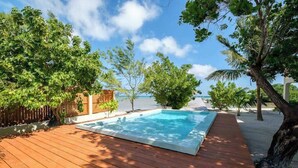 A wooden deck with a swimming pool, surrounded by trees and a view of the sea. - Beachfront abode with well-equipped kitchen - pool, beach, grill, & canoe access (Caye Caulker)