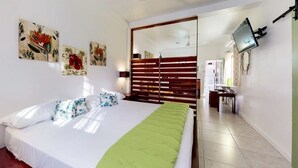 Een slaapkamer met een bed, een plafondventilator, een aan de muur bevestigde televisie en kunst aan de muur.