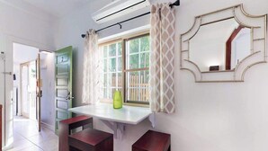 Een kamer met een raam, een spiegel, een groene kast en een witte tafel met twee krukken.