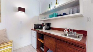 Een compacte kitchenette met een magnetron, koffiezetapparaat en spoelbak. Er is een kleine koelkast en een plank met glazen.