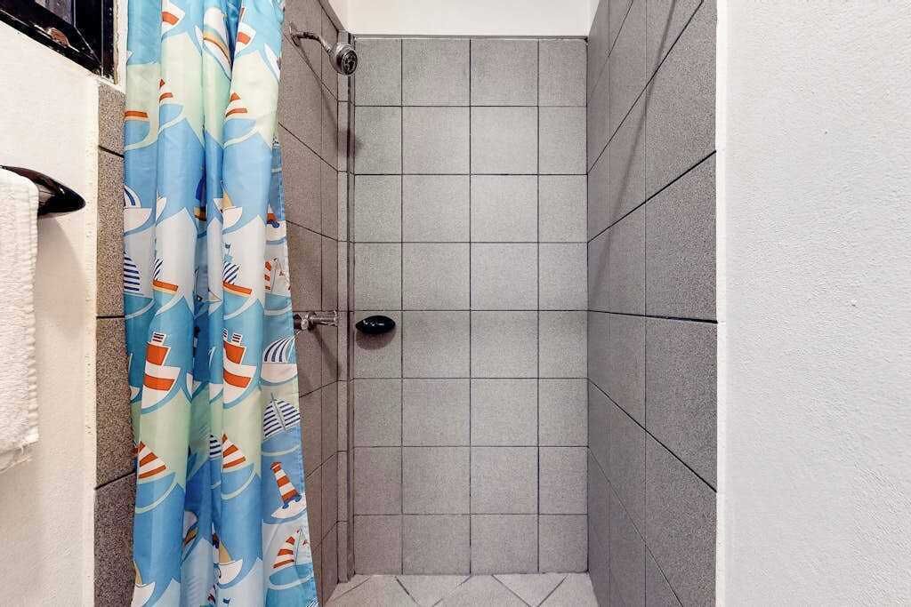 A shower with grey tiles, a blue shower curtain with nautical patterns, and a white towel on the wall.