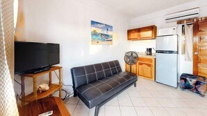 A living room with a sofa, TV, and kitchen area including a fridge and fan. - Unit 8 Muyal Suite at Mayan Falls (Caye Caulker)