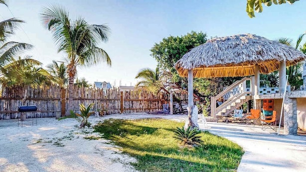A thatched-roof gazebo, a staircase leading to a covered area, and a fenced yard with palm trees. - Unit 8 Muyal Suite at Mayan Falls (Caye Caulker)
